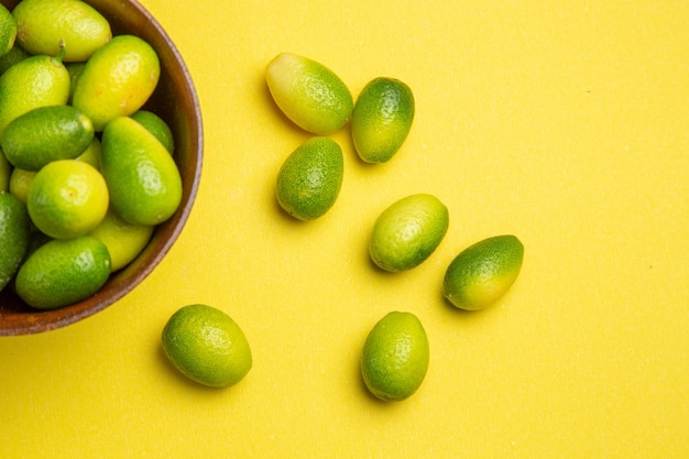 Vista superior de cerca frutas frutas verdes y cuenco marrón sobre la mesa amarilla