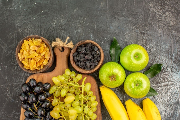 Vista superior de cerca frutas manzanas plátanos cuencos de frutos secos y uvas en la tabla de madera