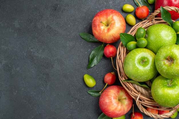 Vista superior de cerca frutas manzanas rojas cerezas frutas cítricas alrededor de la canasta