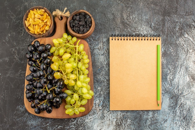 Foto gratuita vista superior de cerca frutas secas cuaderno lápiz uvas en la tabla de madera dos tazones de frutas secas