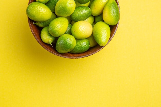 Vista superior de cerca frutas en un tazón sobre la mesa amarilla frutas verdes en el tazón