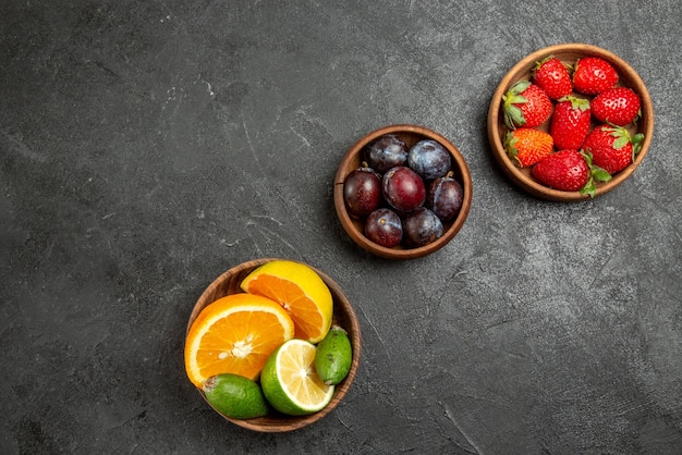 Vista superior de cerca frutas en tazones de mesa de apetitosas bayas y frutas cítricas en la superficie oscura