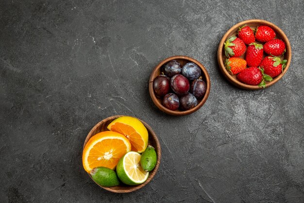 Vista superior de cerca frutas en tazones de mesa de apetitosas bayas y frutas cítricas en la superficie oscura