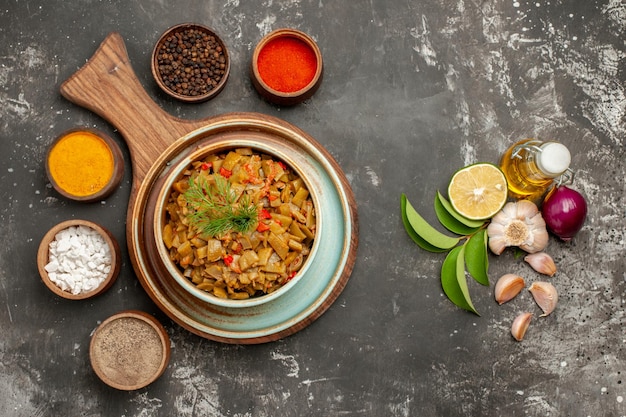 Vista superior de cerca judías verdes con tomates tomates y judías verdes en el plato y tres tipos de especias junto a la botella de aceite ajo cebolla limón y hojas