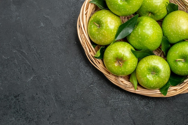 Vista superior de cerca manzanas en la cesta cesta de madera de las manzanas verdes con hojas sobre la mesa oscura