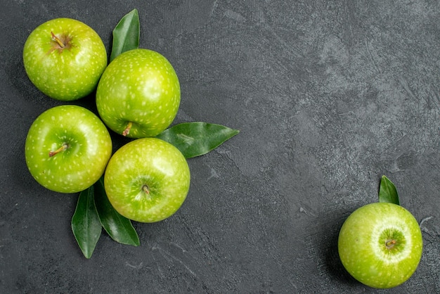 Vista superior de cerca manzanas cuatro manzanas verdes con hojas junto a la manzana en la mesa oscura