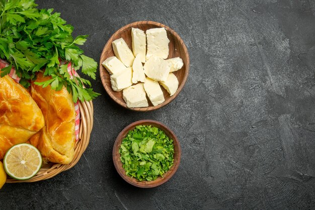 Vista superior de cerca queso hierbas apetitosas tartas de limón y hierbas y mantel a cuadros en la canasta de madera y cuencos de hierbas y queso