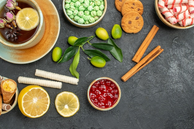 Vista superior de cerca una taza de té, galletas, una taza de té, caramelos de colores, frutas cítricas, palitos de canela