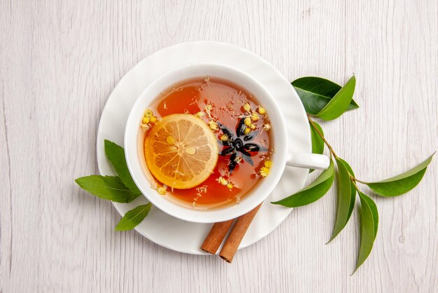 Vista superior de cerca té de hierbas una taza de té de hierbas con palitos de canela y limón en el platillo blanco y hojas de té