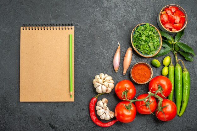 Vista superior de cerca tomates cuaderno lápiz junto a los cuencos de verduras coloridas especias hierbas