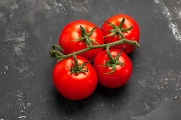 Vista superior de cerca tomates cuatro apetitosos tomates maduros con tallos sobre la mesa negra
