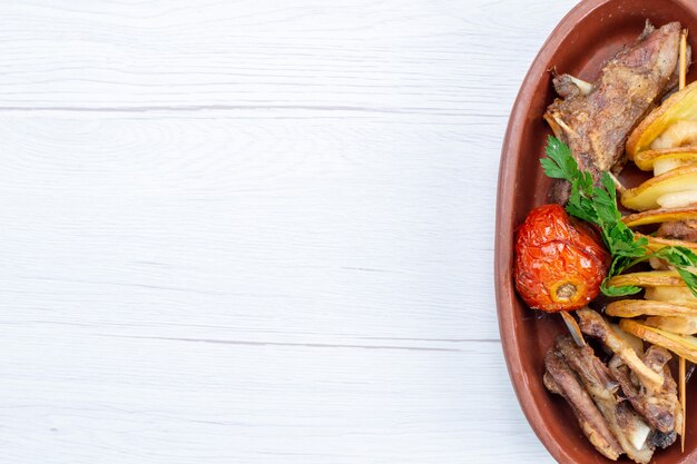 Vista superior cercana de carne frita con verduras y ciruelas al horno dentro de la placa marrón en el escritorio de luz, cena de plato de carne de comida