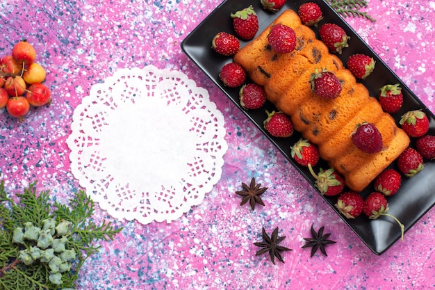 Vista superior cercana delicioso pastel horneado dentro de un molde negro con fresas rojas frescas en el escritorio rosa.