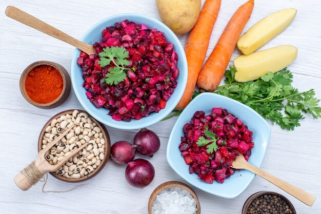 Vista superior cercana de ensalada de remolacha fresca con verduras en rodajas dentro de placas azules con ingredientes en el escritorio de luz, ensalada de verduras comida comida saludable snack