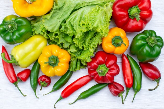 Vista superior cercana de ensalada verde junto con pimientos morrones y pimientos picantes en el escritorio blanco, ingrediente de comida vegetal