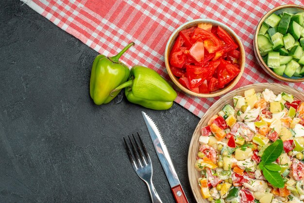 Vista superior cercana de ensalada de verduras en una servilleta roja con verduras y cubiertos sobre fondo gris