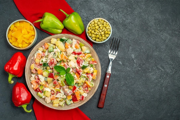 Vista superior cercana de ensalada de verduras en una servilleta roja con verduras y tenedor sobre fondo gris oscuro