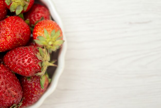 Vista superior cercana de fresas rojas frescas bayas suaves y deliciosas dentro de la placa blanca a la luz, color rojo baya de la foto de la fruta