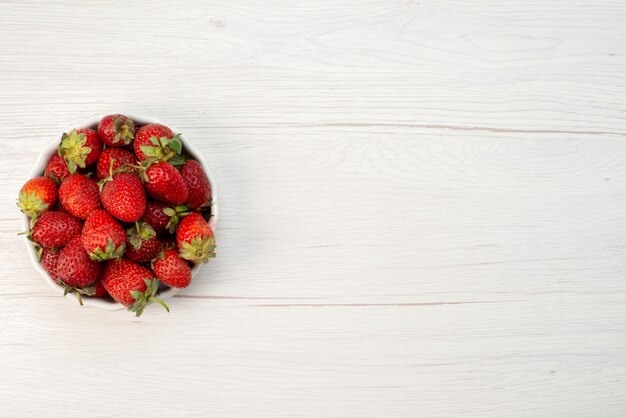 Vista superior cercana de fresas rojas frescas bayas suaves y deliciosas dentro de un plato blanco a la luz, baya de frutas en color rojo fresco