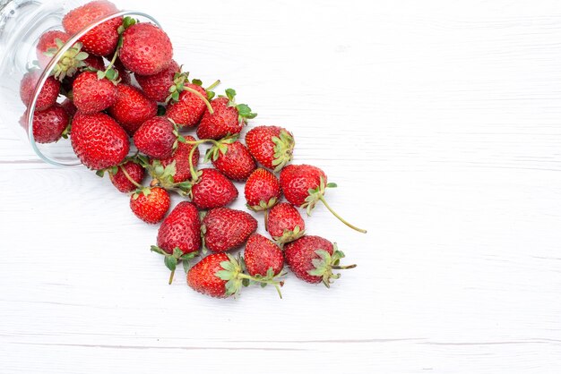 Vista superior cercana de fresas rojas frescas dentro y fuera de la placa en blanco, fruta baya fresca suave