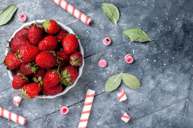 Foto gratuita vista superior cercana de fresas rojas frescas dentro de la placa junto con caramelos de palo en gris, fruta baya dulce dulce