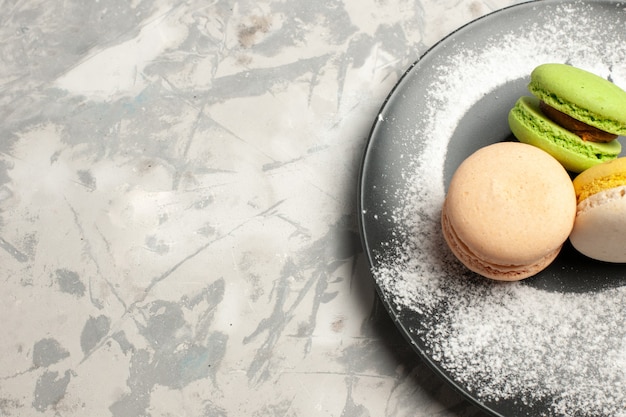 Vista superior cercana macarons franceses deliciosos pasteles de colores dentro de la placa en la superficie blanca