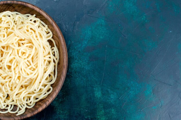 Vista superior cercana pasta italiana cocida dentro de la placa de madera redonda en la pared azul pasta italia comida cena masa carne