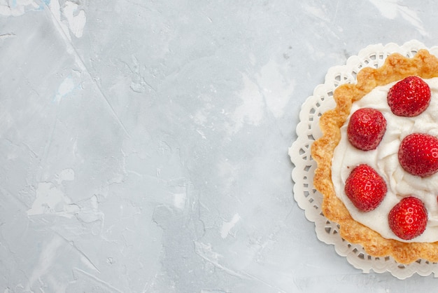 Vista superior cercana del pequeño pastel delicioso con crema y fresas rojas frescas en la mesa de luz