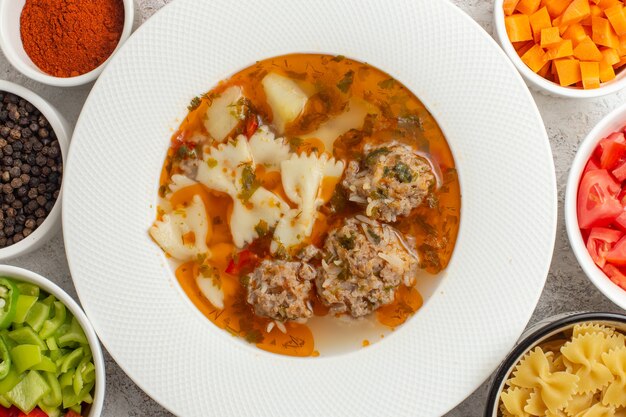 Vista superior cercana sopa con carne deliciosa sopa con verduras en rodajas y diferentes condimentos en la superficie blanca