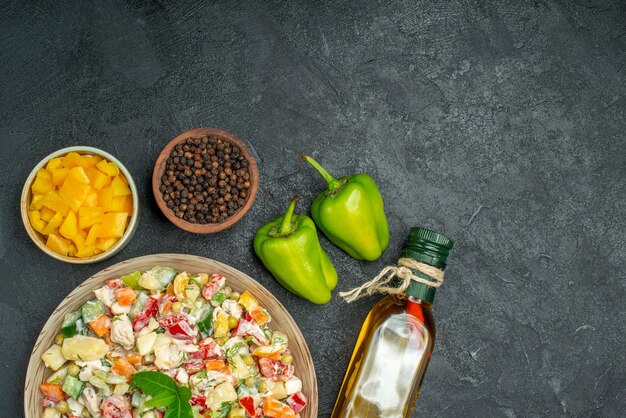 Vista superior cercana del tazón de fuente de ensalada de verduras con tazones de verduras y botella de aceite de pimienta y pimientos en el lado sobre fondo gris