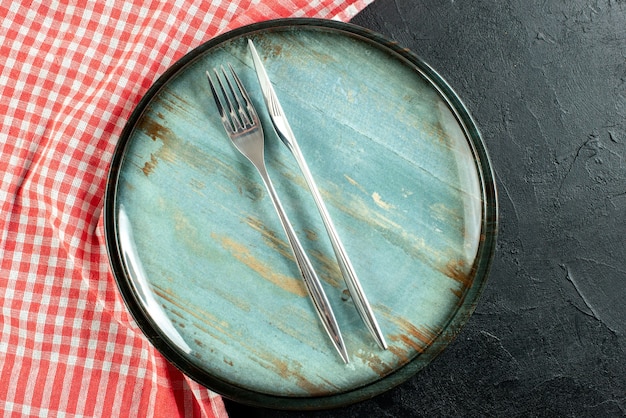 Foto gratuita vista superior cercana tenedor de acero y cuchillo de cena en plato redondo mantel a cuadros rojo y blanco sobre mesa negra