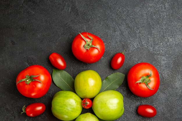 Vista superior cercana tomates rojos y verdes hojas de laurel alrededor de un tomate cherry en la parte inferior del suelo oscuro con espacio de copia