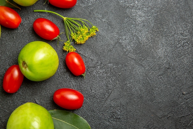 Vista superior cercana de tomates verdes y tomates cherry, flores de eneldo y hojas de laurel a la izquierda del suelo oscuro con espacio de copia