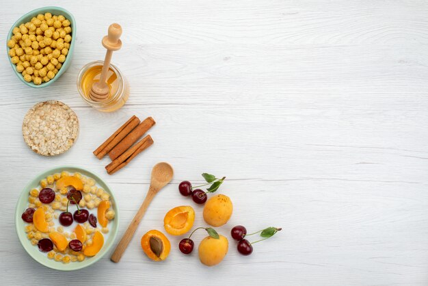 Vista superior de cereales con leche en el interior del plato con galletas de canela, frutas y miel en blanco, beber leche, leche, leche, desayuno