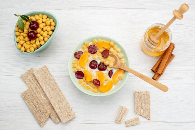 Vista superior de cereales con leche en el interior del plato con galletas y miel en blanco, beber leche leche cremosa