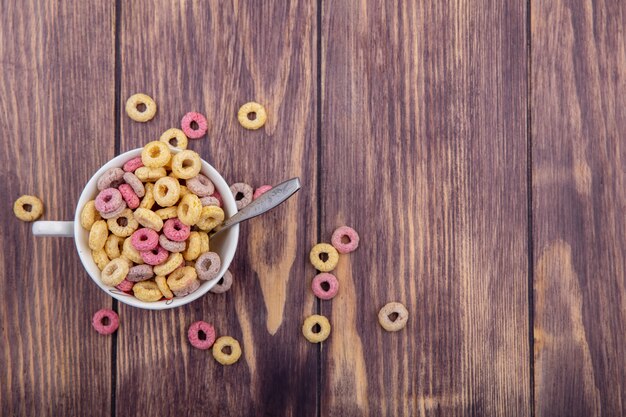 Vista superior de cereales multicolores en un tazón con cuchara con cereales aislados en superficie de madera