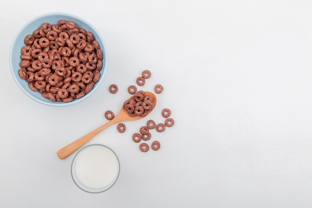 Vista superior de cereales en un tazón y una cuchara de madera con leche sobre fondo blanco con espacio de copia