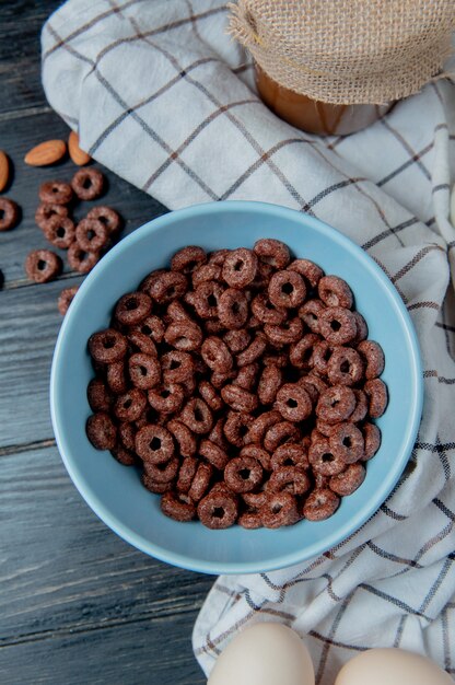 Vista superior de cereales en un tazón con mantequilla de maní y huevos sobre tela escocesa y mesa de madera