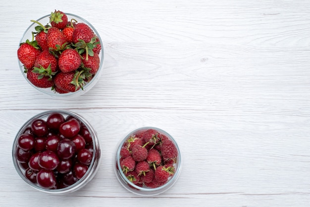 Vista superior de las cerezas ácidas rojas frescas enteras y suaves con fresas y frambuesas en la mesa de luz fruta color fresco amargo suave jugoso