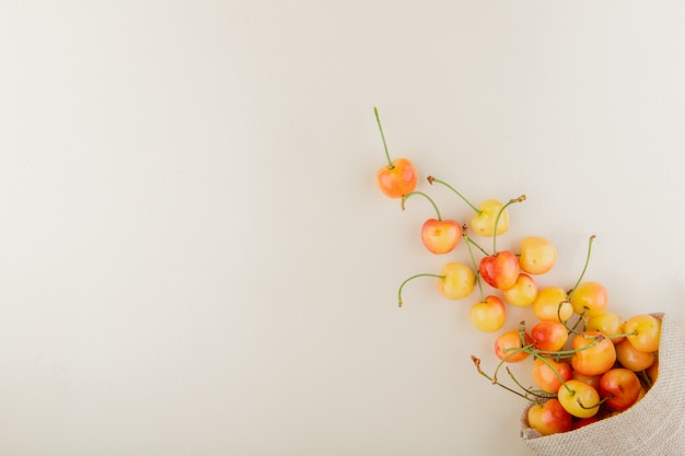 Foto gratuita vista superior de cerezas amarillas derramándose de saco en el lado derecho y mesa blanca