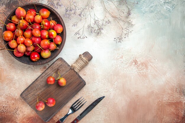 Vista superior de cerezas bayas en el plato de cocina tazón de cerezas ramas de árboles tenedor cuchillo