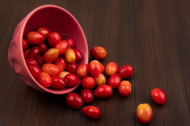 Vista superior de las cerezas de cornalina agria de color rojo pálido cayendo de un recipiente sobre una superficie de madera