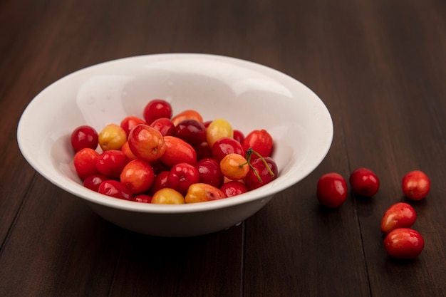 Foto gratuita vista superior de cerezas de cornalina roja en un recipiente blanco sobre una superficie de madera