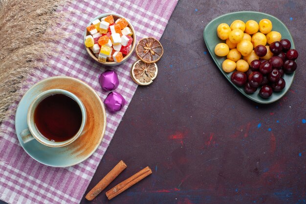 Vista superior de cerezas dulces frescas dentro de la placa con dulces y té de canela en la superficie oscura