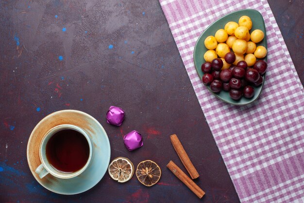 Vista superior de cerezas dulces junto con canela y una taza de té en la superficie oscura