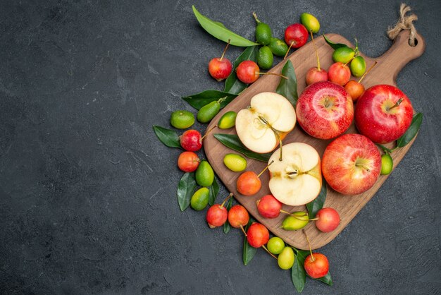 Vista superior de cerezas frutas lejanas alrededor de manzanas con hojas en la tabla de cortar