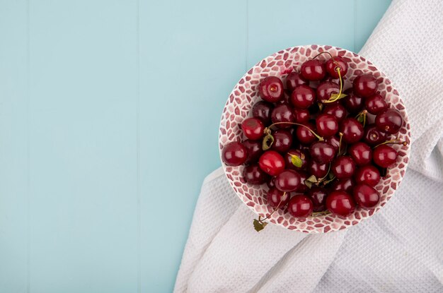 Vista superior de las cerezas en un recipiente sobre un paño blanco sobre fondo azul con espacio de copia