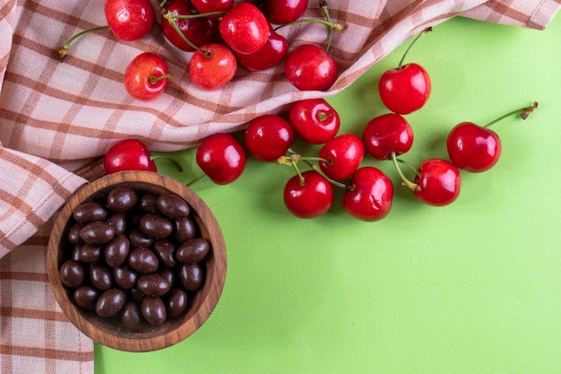 Vista superior cerezas rojas con bombones y una toalla de cocina en verde claro