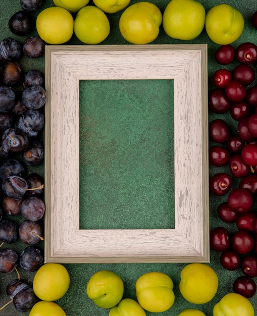 Vista superior de cerezas rojas con endrinas de color púrpura oscuro con ciruelas cereza verde sobre un fondo verde con espacio de copia