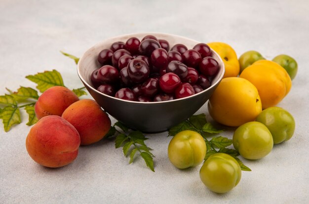 Vista superior de cerezas rojas en un recipiente negro con melocotones frescos y jugosos con ciruelas cereza verde aislado sobre un fondo blanco.